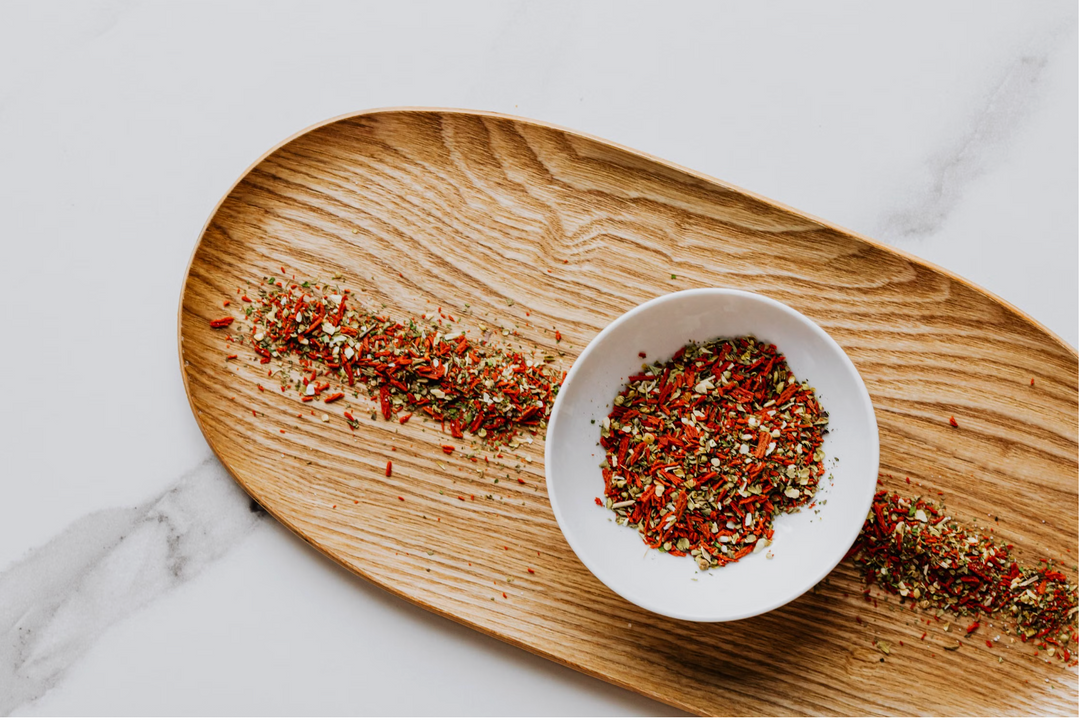 Organic grilling spice rubs in small bowls beside raw meat and vegetables