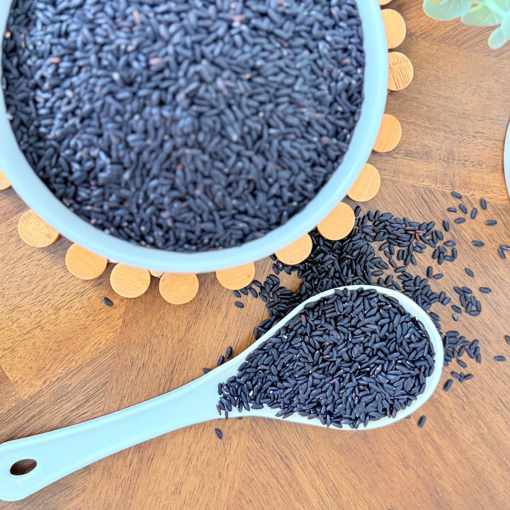 A bowl of uncooked organic black rice, rich in natural pigments, perfect for adding color, texture, and nutrition to a variety of dishes."