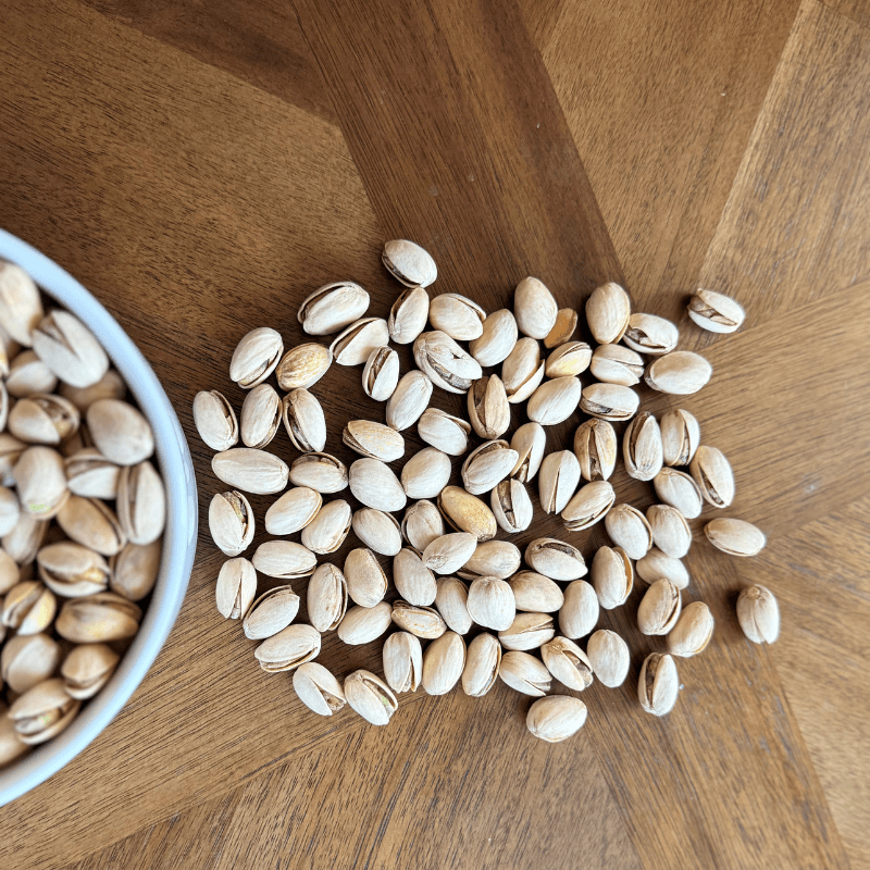 Organic pistachios from Purely Organic Foods, roasted to perfection and salted, displayed with open shells revealing vibrant green nuts inside."

"Bowl of organic roasted pistachios with split shells, seasoned with sea salt, perfect as a premium-quality plant-based snack option."